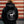 A person viewed from behind wearing a black hoodie with a large white circular graphic on the back that reads '9 Line Farms Wagyu' and shows a cow silhouette. The background is a rustic wooden wall with horizontal red and beige wood planks.