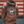 A person viewed from behind wearing a brown hoodie with a large circular farm graphic on the back that reads '9 Line Farms Wagyu Wagyu Farm Wagyu' and 'Wagyu, Florida.' The background shows a red, white, and gray striped wall.