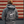 A person shown from behind wearing a dark gray hoodie with a large white circular graphic on the back that reads '9 Line Farms Wagyu' and 'Sonita, Florida,' standing in front of a rustic red-and-beige wood plank wall.