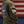 A person wearing an olive green hoodie, shown from the back and side. The hoodie features a large white circular '9 Line Farm Wagyu' graphic on the back and a white American flag patch on the sleeve.